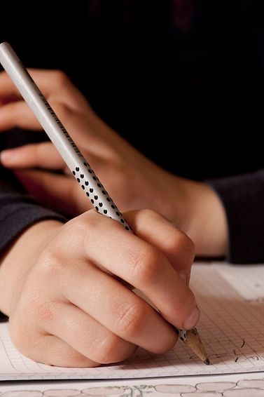 Eine Kinderhand schreibt mit Bleistift in ein Schulheft.